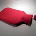 Un sac rouge chauffant posé sur un sol blanc, capuchon à côté