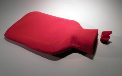 Un sac rouge chauffant posé sur un sol blanc, capuchon à côté