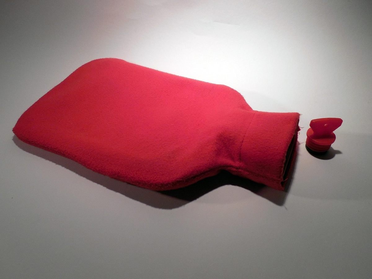 Un sac rouge chauffant posé sur un sol blanc, capuchon à côté