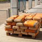 Des palettes de sacs orange empilés sur un sol bétonné à l'extérieur