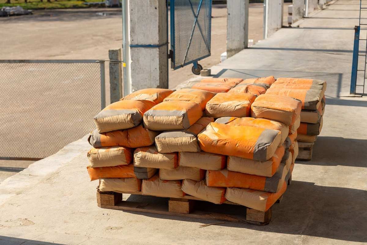 Des palettes de sacs orange empilés sur un sol bétonné à l'extérieur