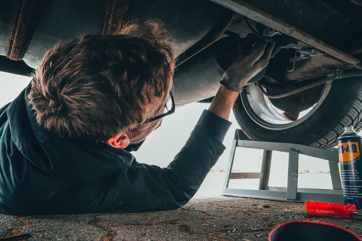 Homme sous un véhicule, manipulant la suspension avec des outils à proximité