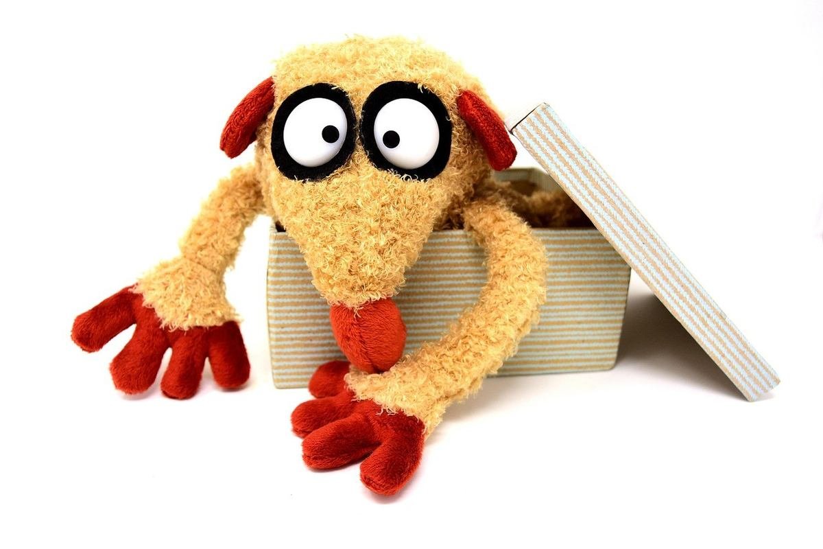 Peluche anthropomorphe aux yeux exagérés sortant d'une boîte en carton