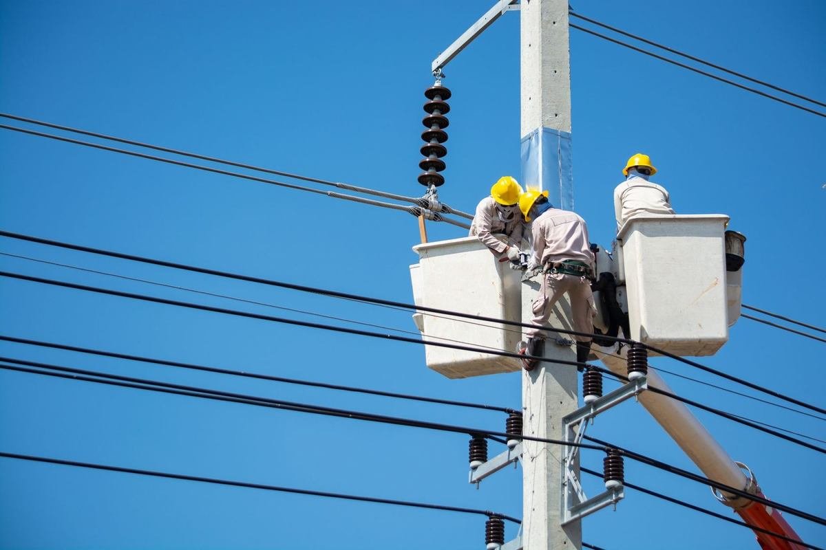 Techniciens en paniers-cage sur une tour électrique, manipulant des câbles